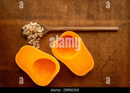 Zwei Hälften geschnitten Reif butternut squash mit Saatgut und vintage Holzlöffel auf rustikalen hölzernen Tischplatte von oben Stockfoto