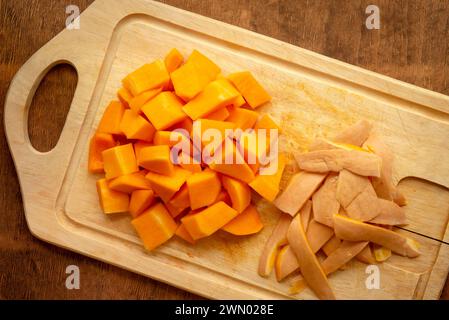 Stücke geschnittener Butternusskürbis und Schneidebrett auf rustikaler Holzplatte von oben Stockfoto