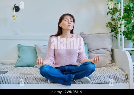 Reife Frau betet, meditiert, sitzt zu Hause auf der Couch Stockfoto