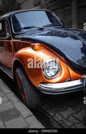 Oldtimer in der urbanen Altstadt. Nahaufnahme eines glänzenden orangen Retro-Autos. Oldtimer-Detail Vorne. Nahaufnahme des Scheinwerfers Retro Oldtimer. Straßenfoto, Stockfoto