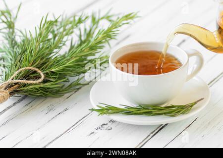 Glasschale gesunder Rosmarintee mit frischem Rosmarinbunch auf rustikalem Hintergrund, winterliches Kräuter-Heißgetränk-Konzept, salvia rosmarinus Stockfoto