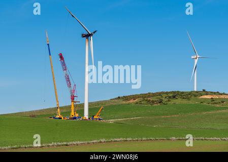 Riesige Kräne neben einer Windturbine, die einen Brand erlitten hat, Hochhubkrane, um die beschädigte Turbine und Propeller auszutauschen. Stockfoto