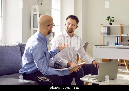 Zwei junge Geschäftsleute, die sich unterhalten, während sie auf dem Sofa im Büro sitzen Stockfoto