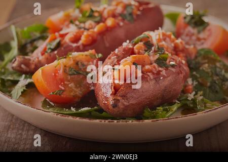 Süße gebackene Kartoffeln mit Bohnen und geriebenem Käse, mit Spinat und Rucolasalat. Stockfoto