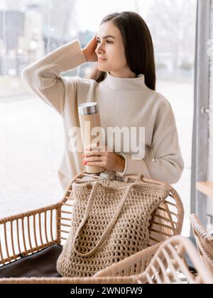 Junge attraktive Frau mit Thermoskanne, die sich im Café entspannt Stockfoto