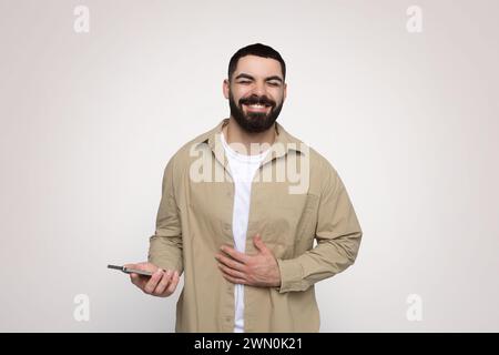Glücklicher bärtiger Mann, der ein Smartphone hält und sein Herz berührt Stockfoto
