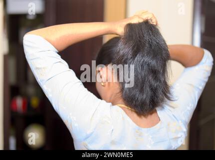 Eine junge asiatische Frau mit einem konzentrierten Ausdruck streckt ihren Hals in ihrem sonnendurchfluteten Wohnzimmer und beginnt ihren Tag mit einem Fokus auf Wellness. Stockfoto