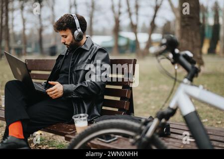 Hübscher Geschäftsmann, der im Park mit dem Fahrrad an einem Laptop arbeitet. Stockfoto