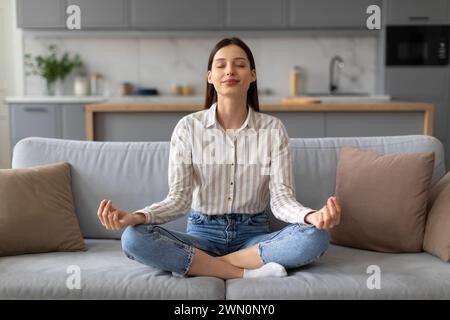 Frau, die zu Hause auf der Couch Meditation übt Stockfoto