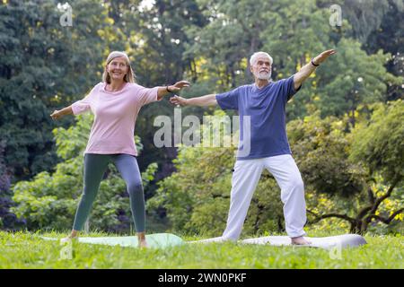 Ein reifer Mann und eine Frau, die Yoga in einem ruhigen Park durchführen, in dem Gesundheit und Zweisamkeit in der Natur leben. Stockfoto
