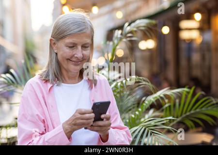 Glückliche reife Frau in lässiger Kleidung mit Mobiltelefon mit Content Lächeln, Technologie und Freizeitkonzept. Stockfoto