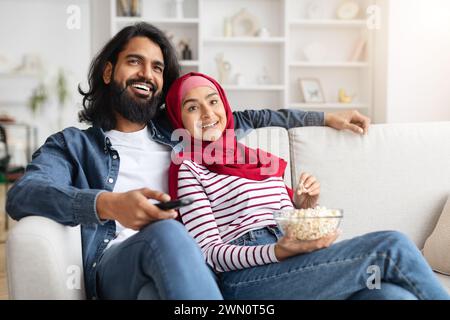 Entspanntes muslimisches Paar, das sich auf der Couch mit Popcorn-Schüssel entspannt Stockfoto