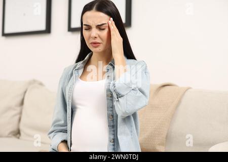 Schwangere junge Frau mit Kopfschmerzen in Innenräumen Stockfoto