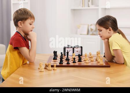 Niedliche Kinder, die Schach am Tisch im Zimmer spielen Stockfoto
