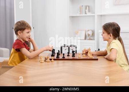 Niedliche Kinder, die Schach am Tisch im Zimmer spielen Stockfoto