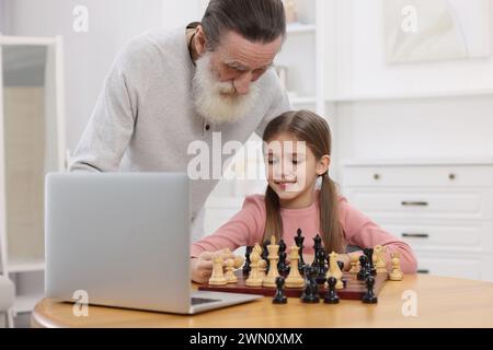 Großvater bringt seiner Enkelin Schach bei, nachdem er zu Hause online unterrichtet wurde Stockfoto