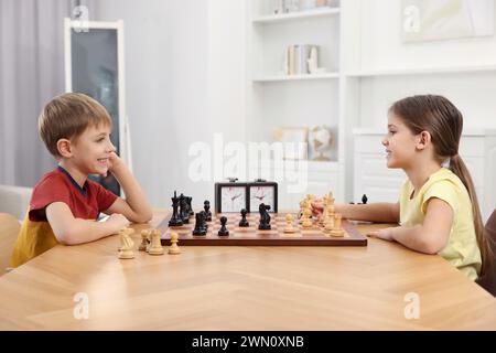 Niedliche Kinder, die Schach am Tisch im Zimmer spielen Stockfoto