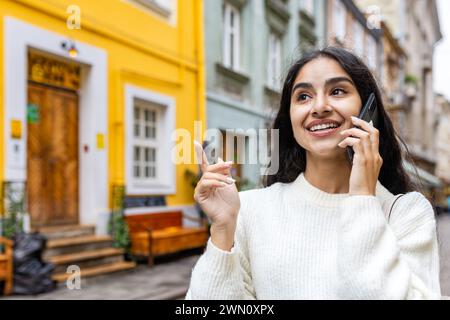 Ein Nahfoto einer lächelnden Indianerin, die durch die Stadt geht und mit einem Handy spricht. Stockfoto