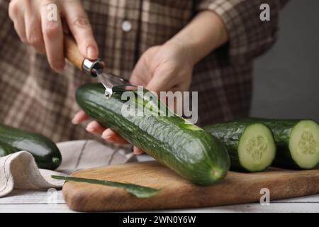 Frau, die frische Gurke am weißen Holztisch schält, Nahaufnahme Stockfoto