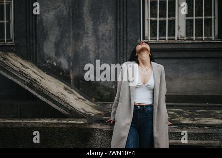 Ein junges, stilvolles Teenager-Mädchen mit Sonnenbrille macht einen gemütlichen Spaziergang und genießt an einem Herbsttag die kühle Atmosphäre der Stadt. Stockfoto