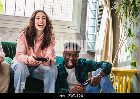 Eine junge Frau und ein Mann brachen in Lachen aus, während sie an einer Videospielsession teilnahmen, in einem wohnlichen Raum mit natürlichem Licht Stockfoto