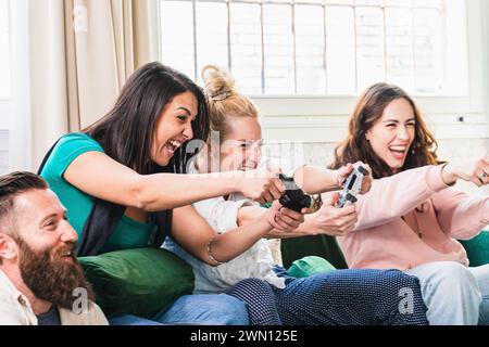 Eine überschwängliche Gruppe von Freunden ist in einem Moment verspielter Wettkämpfe gefangen und genießt auf einer bequemen Couch einen lebhaften Videospielkampf Stockfoto