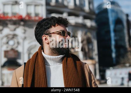 Outdoor-Porträt eines stilvollen bärtigen Mannes, der Sonnenbrille und Winterkleidung trägt und glücklich und sorglos in einer städtischen Umgebung aussieht. Stockfoto