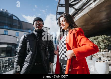 Professionelles multiethnisches Geschäftsteam, das im Freien arbeitet. Stilvolle Frau im roten Mantel und Mann in Beanie, die unterwegs Papierkram lesen. Stockfoto