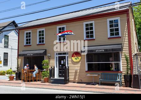 Eine reizvolle Straßenszene tagsüber in der AVAS Pizzeria, in der Sie im Freien speisen und die amerikanische Flagge in einem malerischen Stadtbild genießen können Stockfoto