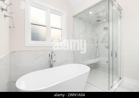 Das Badezimmer verfügt über eine freistehende Badewanne mit Chromarmatur, Marmorfliesen an Wänden und Boden und eine begehbare Dusche mit Marmorwänden und -Bank. Stockfoto