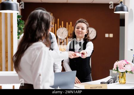 Weibliche Concierge begrüßt und unterstützt ältere Reisende gern und prüft ihre Ausweise für nahtlosen Check-in. An der Rezeption gibt der Mitarbeiter an der Rezeption den Reisepass nach der Bestätigung an die Seniorin zurück. Stockfoto