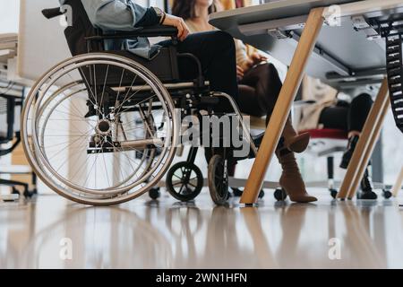 Behinderte männliche Mitarbeiter sitzen im Rollstuhl und diskutieren mit seinen Teamkollegen bei einem Treffen am Tisch. Zugeschnittenes Foto. Stockfoto