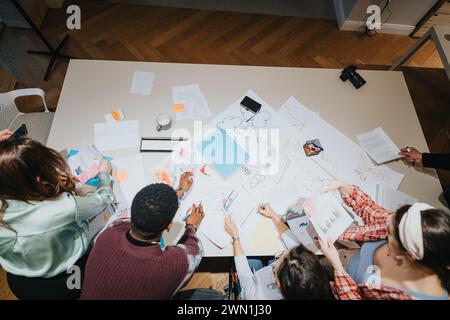 Multirassische Gruppe von Personen, die an einer Brainstorming-Sitzung teilnehmen, mit Unterlagen und Diagrammen auf einem großen Tisch, in denen Teamarbeit und Strategie vorgestellt werden. Stockfoto