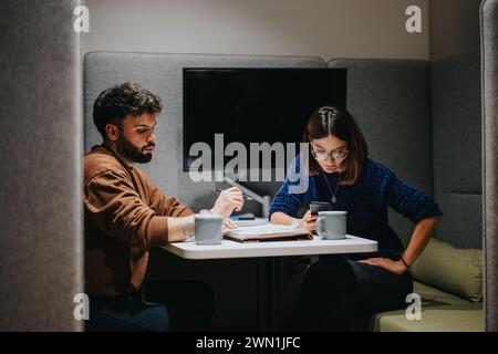 Zwei Kollegen führten ein durchdachtes geschäftliches Gespräch, während sie in einem Büro mit hoher Rückenlehne saßen, mit Dokumenten und Kaffee auf dem Tisch. Stockfoto