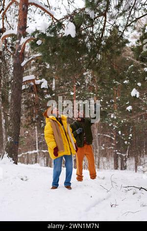 Vertikale Aufnahme eines fröhlichen jungen kaukasischen Paares, das am Wintertag Zeit zusammen im Waldpark verbringt Stockfoto