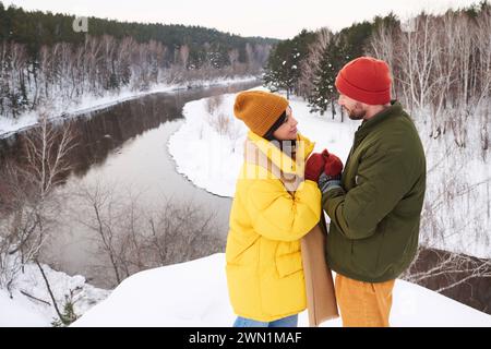 Hochwinkelaufnahme von verliebten jungen Männern und Frauen, die am Wintertag auf einer Klippe stehen und sich gegenseitig die Hände wärmen Stockfoto