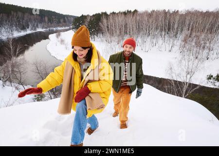 Blick aus einem hohen Winkel auf das aktive junge kaukasische Paar, das am Wintertag an einem malerischen Ort am Fluss wandert Stockfoto