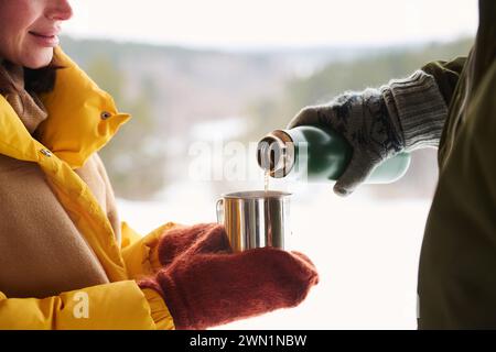 Unerkennbarer Mann mit warmen Handschuhen, der heissen Tee für seine Frau an kalten Wintertagen gießt, mittlere Nahaufnahme Stockfoto