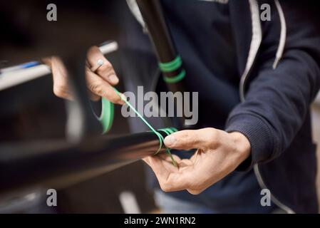 Arbeiter Hände, nicht erkennbarer Mann, der einen Fahrradrahmen mit Abdeckband für ein individuelles Gemälde in seiner Fahrradwerkstatt vorbereitet, ein handgefertigter Kreativ Stockfoto