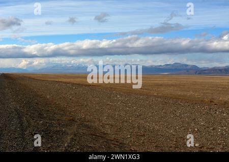 Flache, grenzenlose Steppe mit gelblichem Gras am Fuße einer hohen Bergkette unter einem bewölkten Herbsthimmel am frühen Abend. Stockfoto