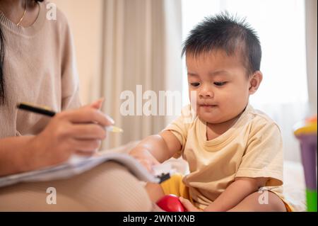 Ein süßer, unschuldiger asiatischer Junge versucht, seine Mutter zu spielen und zu stören, während sie zu Hause arbeitet. Kindheit, kleiner Sohn, Kind Stockfoto