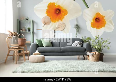 Stilvolle Innenausstattung des Zimmers mit grauem Sofa und wunderschönen Narzissen-Blumen an der Wand Stockfoto