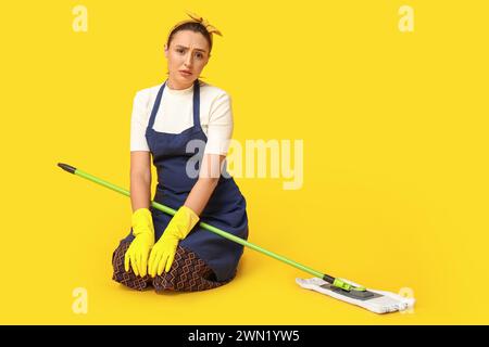 Porträt müder junger Hausfrau in Schürze mit Wischtuch auf gelbem Hintergrund Stockfoto