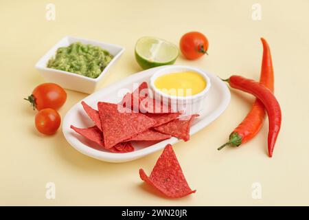 Teller mit roten Nachos, Saucen und Chili auf gelbem Hintergrund Stockfoto