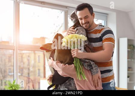 Junger Mann mit Tulpen und seinen kleinen Kindern, der am Ostertag die Militärmutter umarmt Stockfoto