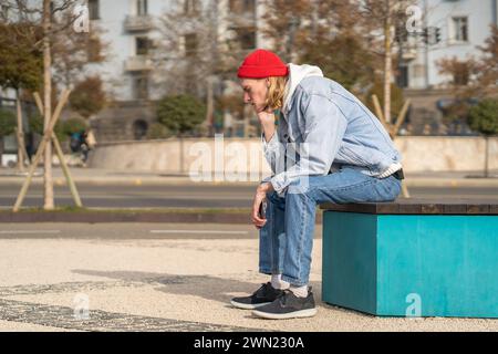 Enttäuschter, trauriger Kerl, der auf der Straße mit dem Handy in Apathie saß, nachdem er schlechte Nachrichten und Nachrichten erhalten hatte Stockfoto