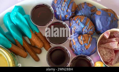 Eine Party-Platte für eine Kindergeburtstag mit bunten süßen Speisen wie Lollies, Süßigkeiten, Gelee und blauen und violetten Plätzchen mit Schokoladenüberzug. Stockfoto