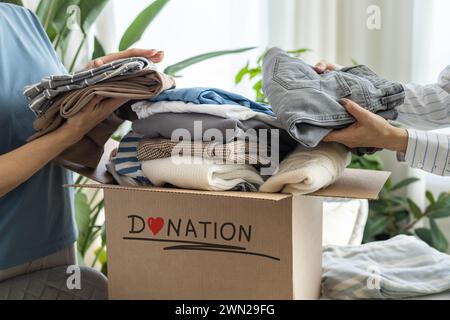 Spendenkonzept. Freiwillige Frauen sammeln Kleidung in einer Spendenbox für wohltätige Zwecke. Stockfoto
