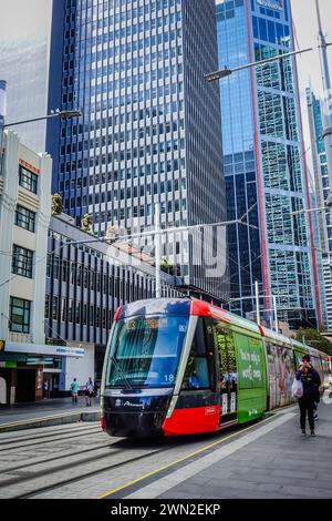 Ein Sydney Light Rail-Zug fährt an einem sonnigen Tag aus einer Station in der George Street in Sydney heraus und erfasst die urbane Szene und die Verkehrsaktivitäten in Stockfoto