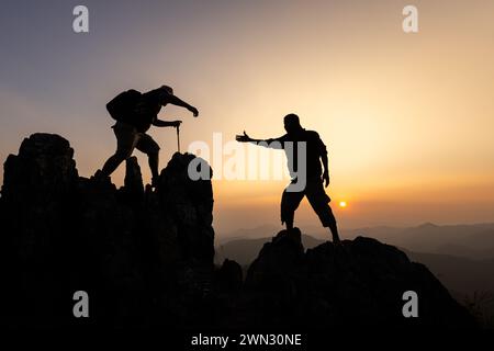 Silhouette der Männer, die dabei helfen, Menschen von hohen Klippen hochzuziehen. Stockfoto